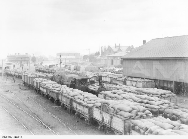 Railway trucks stacked with bagged grain waiting for transport from the railway station at Port Adelaide. Approximately 1910