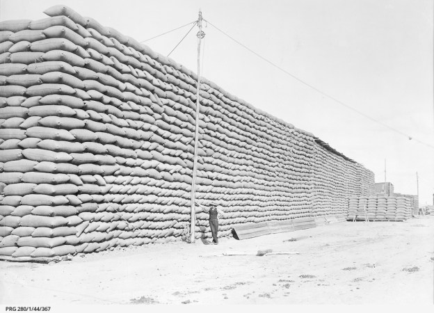 Large stacks of bagged wheat waiting for transportation from a receiving post in South Australia; exact location not known., Approximately1911.