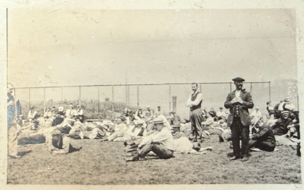 Männer warten auf einer abgezäunten Wiese; Aufnahme von Julius Hagenah, vermutlich auf Ellis Island am 6./7. April 1917; Aufnahme in Privatbesitz, mit freundlicher Genehmigung der Familie